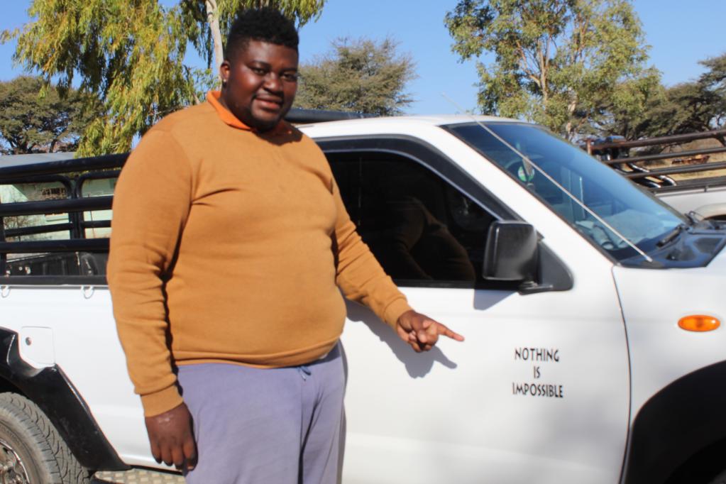A man standing in front of a white car pointing to a nothing is impossible sticker on the side of the car