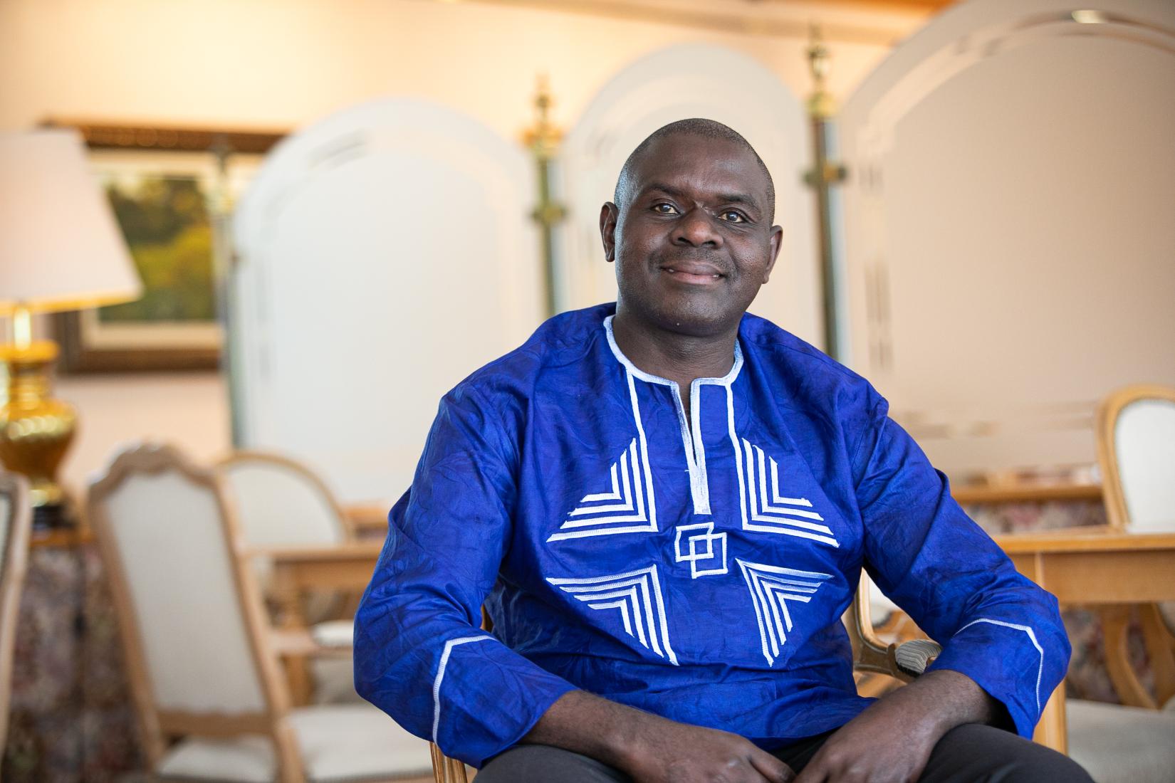 A man seated on a chair in a royal blue shirt