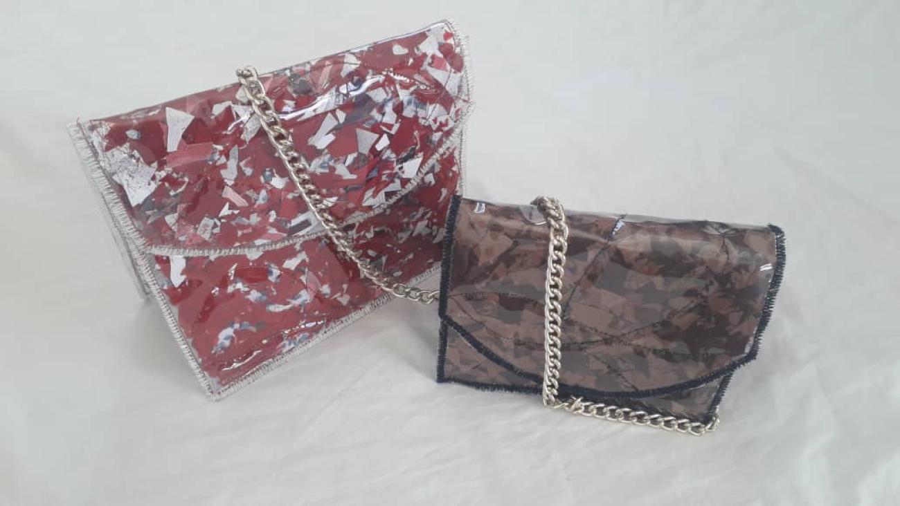 Two clutch bags in front of a white background. One is a red and white clutch bag with a plastic/PVC covering and a metal chain while the other is a brown bag with a plastic/PVC covering, black lining and a metal chain.
