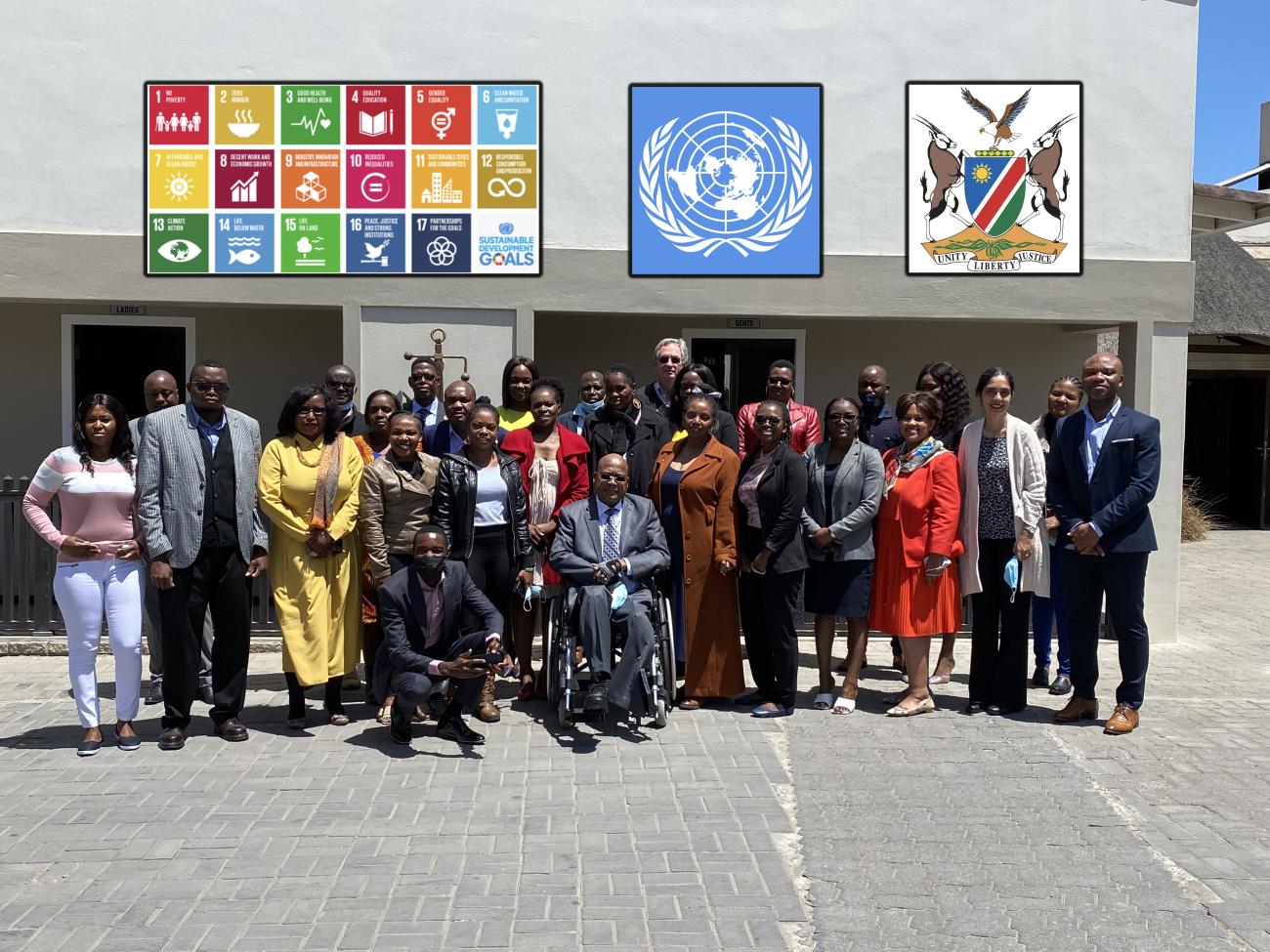 Officials gather for a photo. The UN logo and Namibian coat of arms are imposed above. 