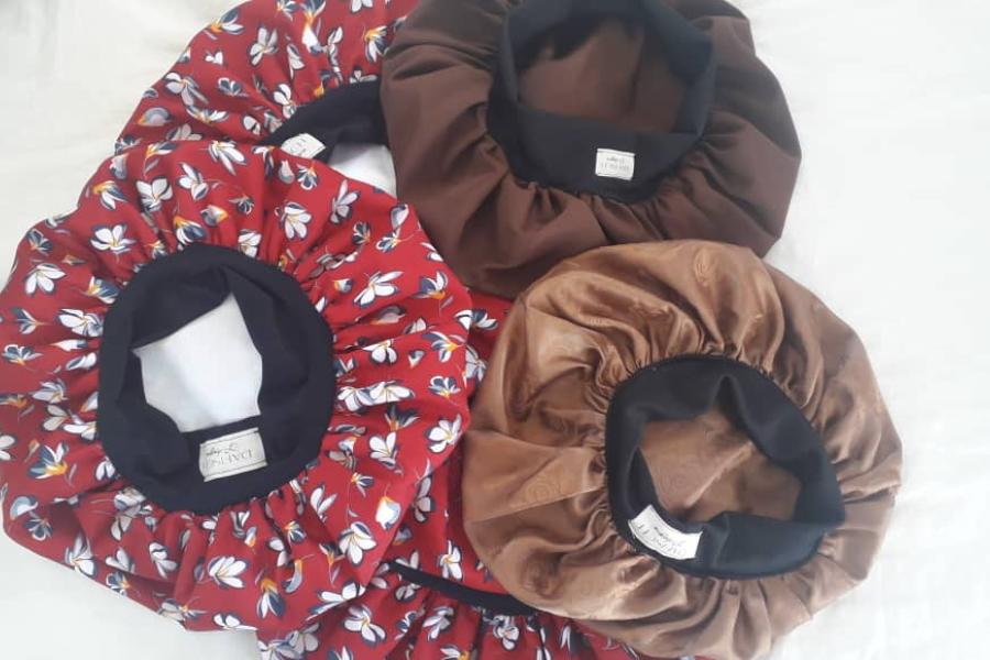 A selection of three bonnets from Shariefa Fisch's DaFisch clothing and accessory line. Featured here are a red printed bonnet, a light brown bonnet and a dark brown bonnet, all of which are lined with a black elastic.