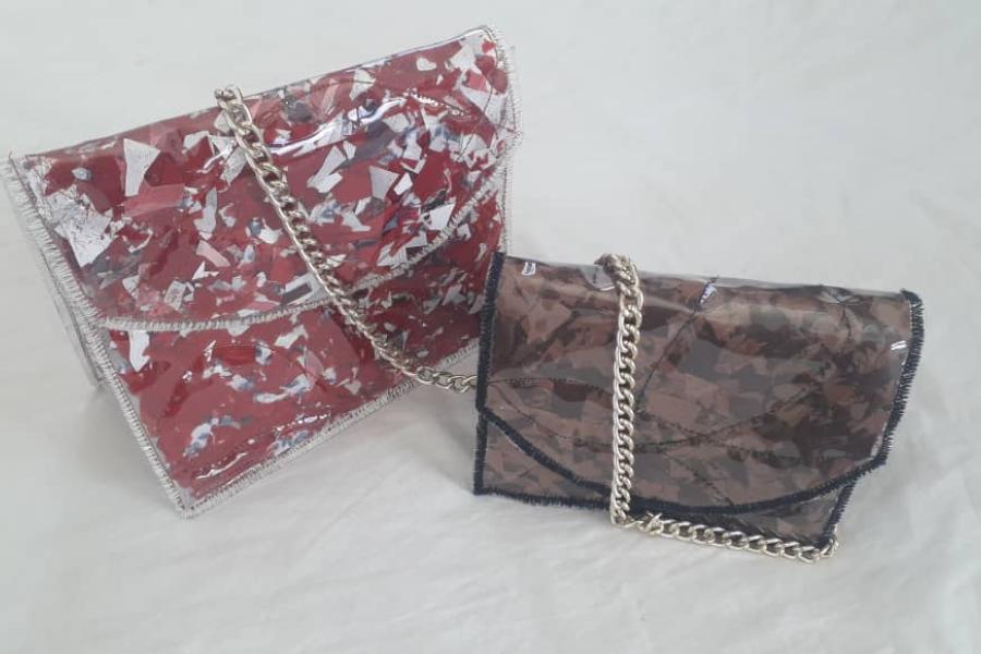 Two clutch bags in front of a white background. One is a red and white clutch bag with a plastic/PVC covering and a metal chain while the other is a brown bag with a plastic/PVC covering, black lining and a metal chain.
